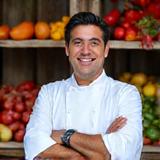 Portrait d'un chef cuisinier péruvien charismatique, en tablier, souriant devant un étal de légumes colorés des Andes.