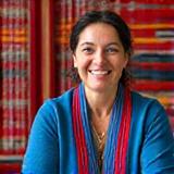 Portrait d'une tisserande berbère souriante, assise devant son métier à tisser traditionnel, entourée de motifs colorés et de tapis berbères.